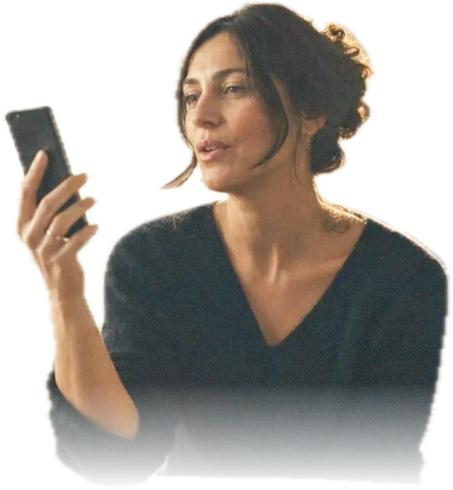 A woman at her kitchen table holding a phone up in front of her, speaking a practice exercise aloud in late afternoon light