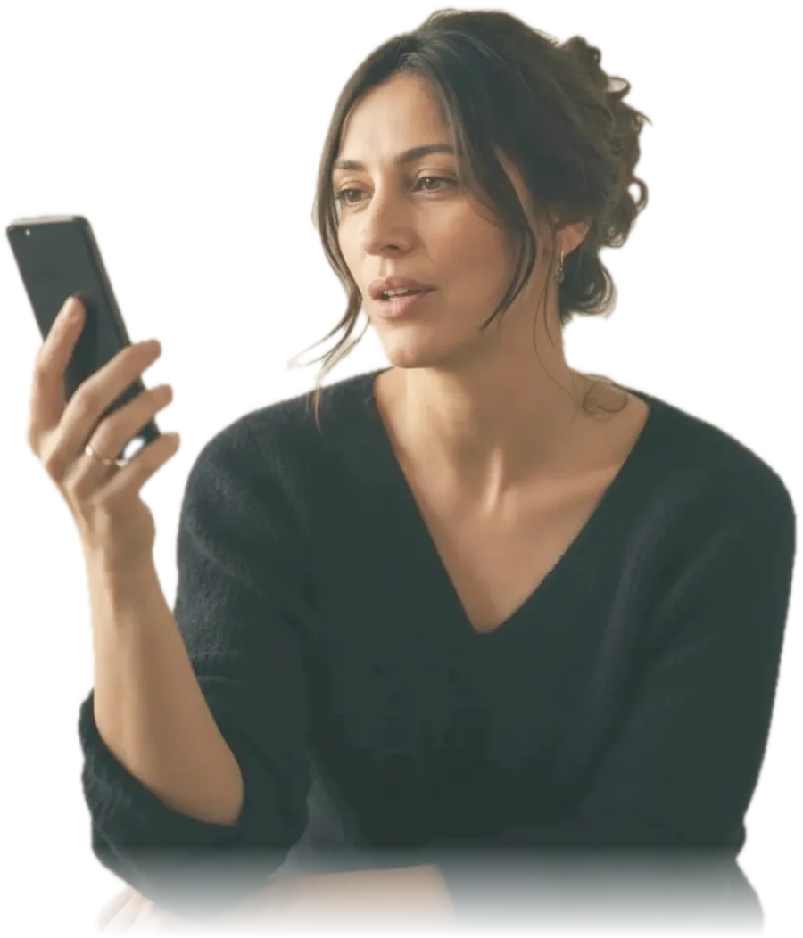 A woman at her kitchen table holding a phone up in front of her, speaking a practice exercise aloud in late afternoon light